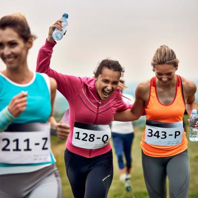 Happy athletic women having fun while running a marathon in nature. Cheerful runners having fun while participating in a race in nature.